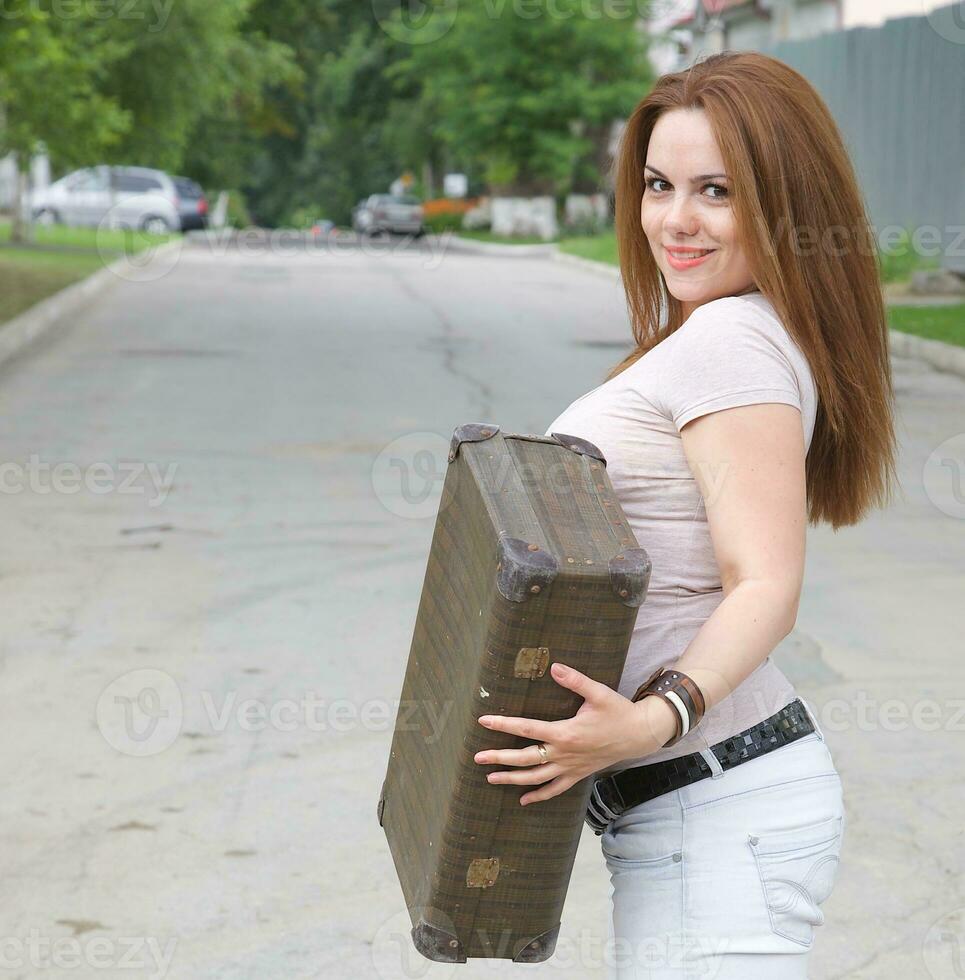 A young attractive woman with an old suitcase on the street photo