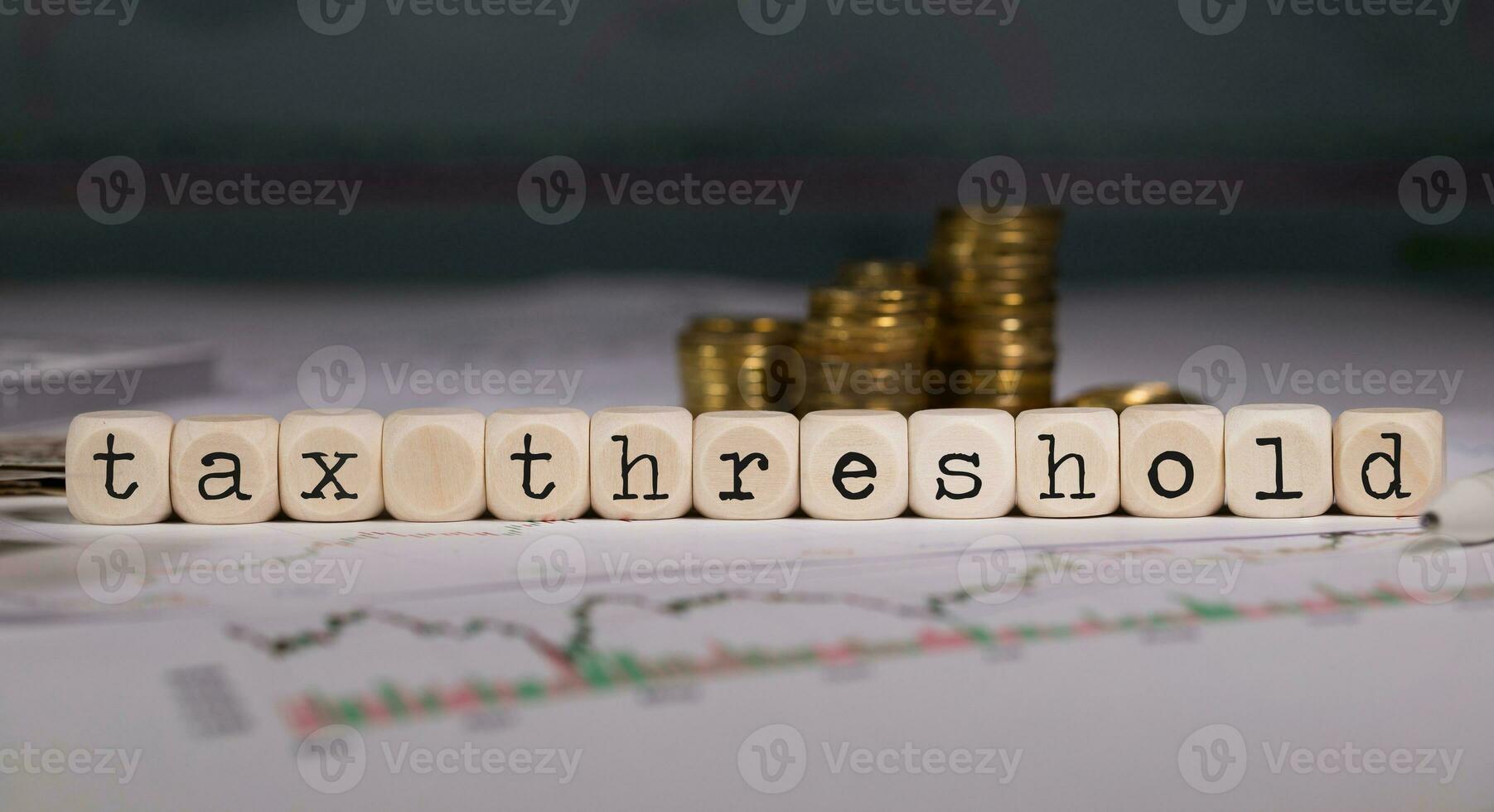 Words TAX THRESHOLD composed of wooden letters. Stacks of coins in the background. photo