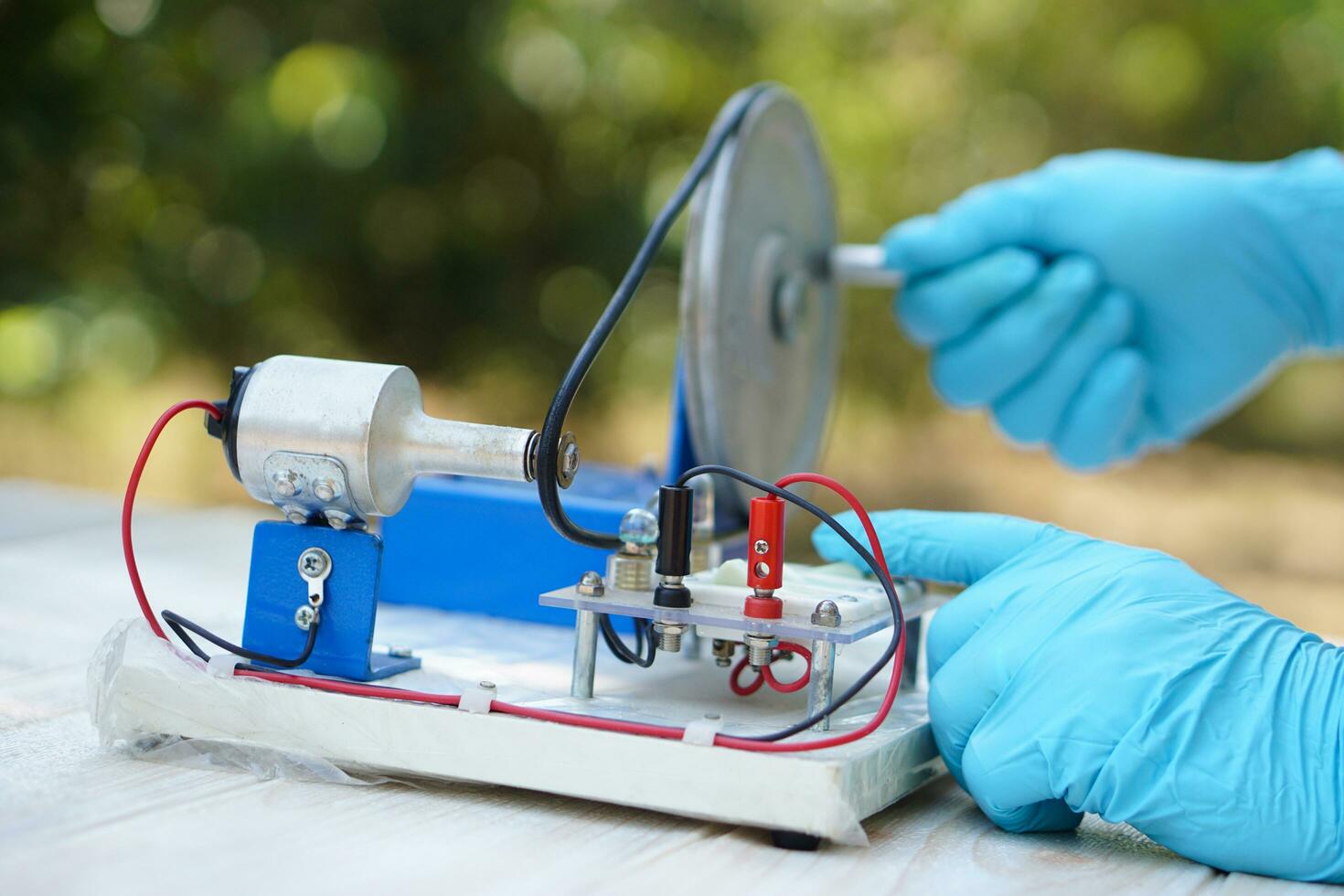 Close up hands wear blue gloves demonstrate science experiment about electricity circuit from dynamo kit for teaching. Concept, science subject, project work. Experiment, education. Outdoor class photo