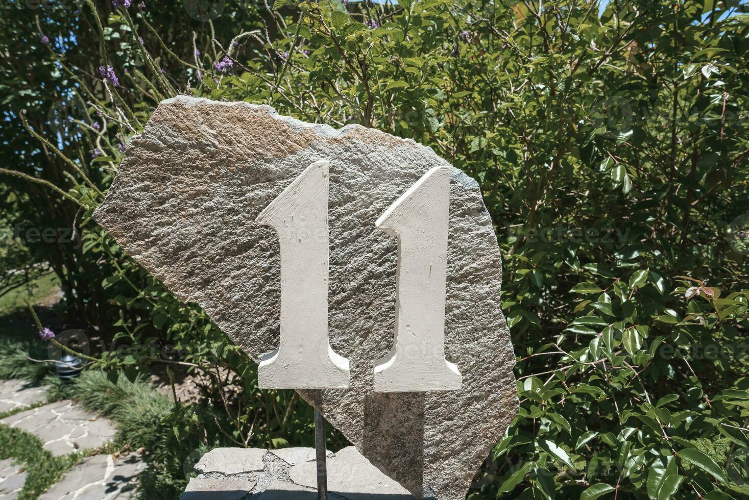 House number 11 installed on a big rock in the garden photo
