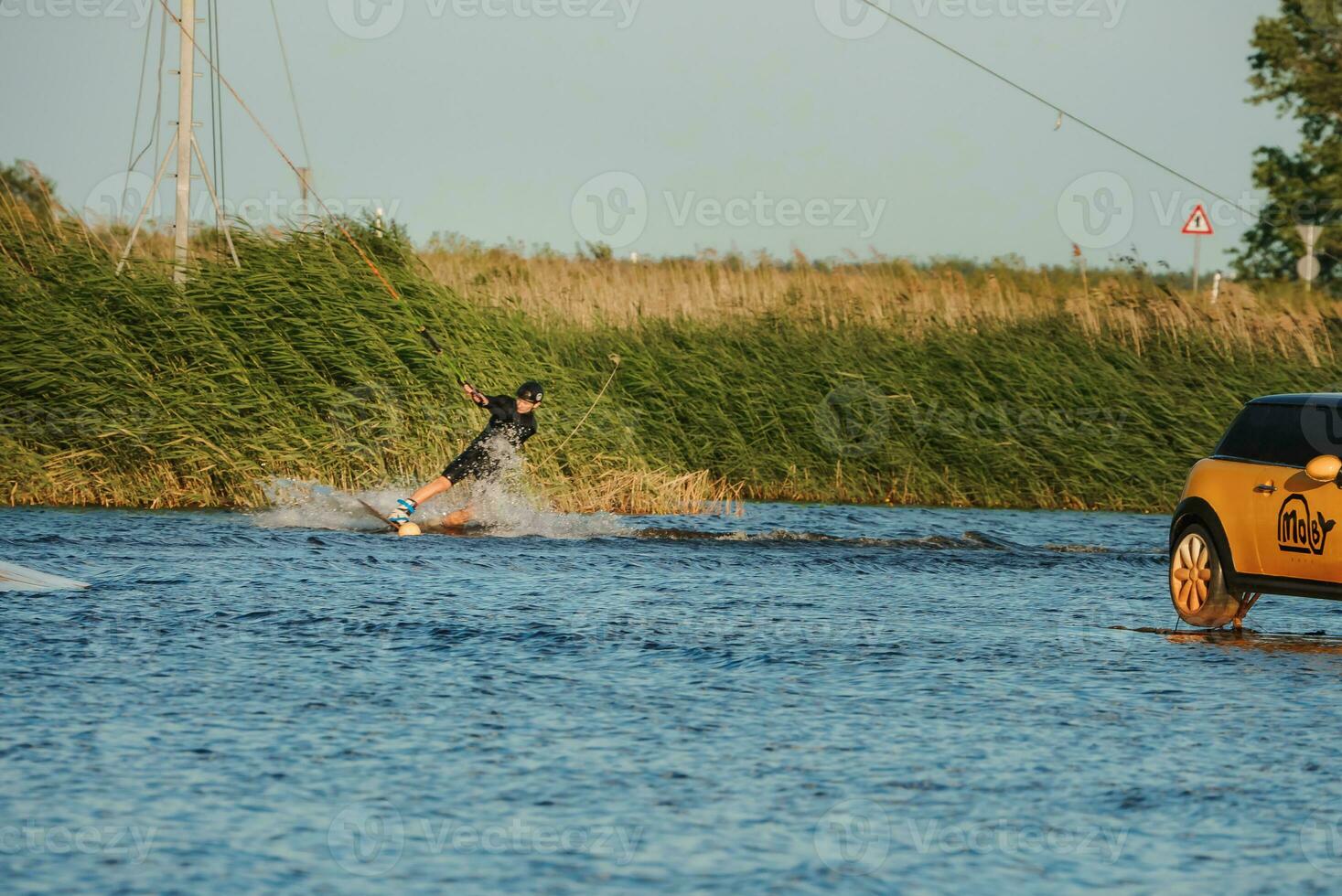 Beautiful view of young man rider holding rope and making extreme jump on wakeboard. Wakeboarding and water sports activity. Low angle shot of man wakeboarding on a lake. Man water skiing at sunset. photo