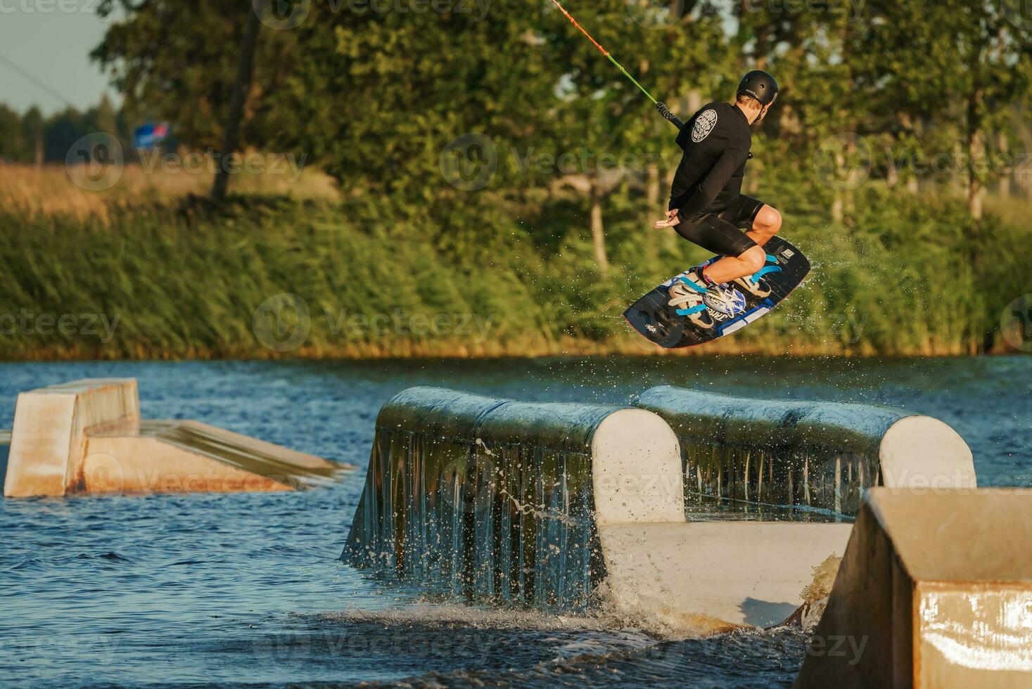 Beautiful view of young man rider holding rope and making extreme jump on wakeboard. Wakeboarding and water sports activity. Low angle shot of man wakeboarding on a lake. Man water skiing at sunset. photo