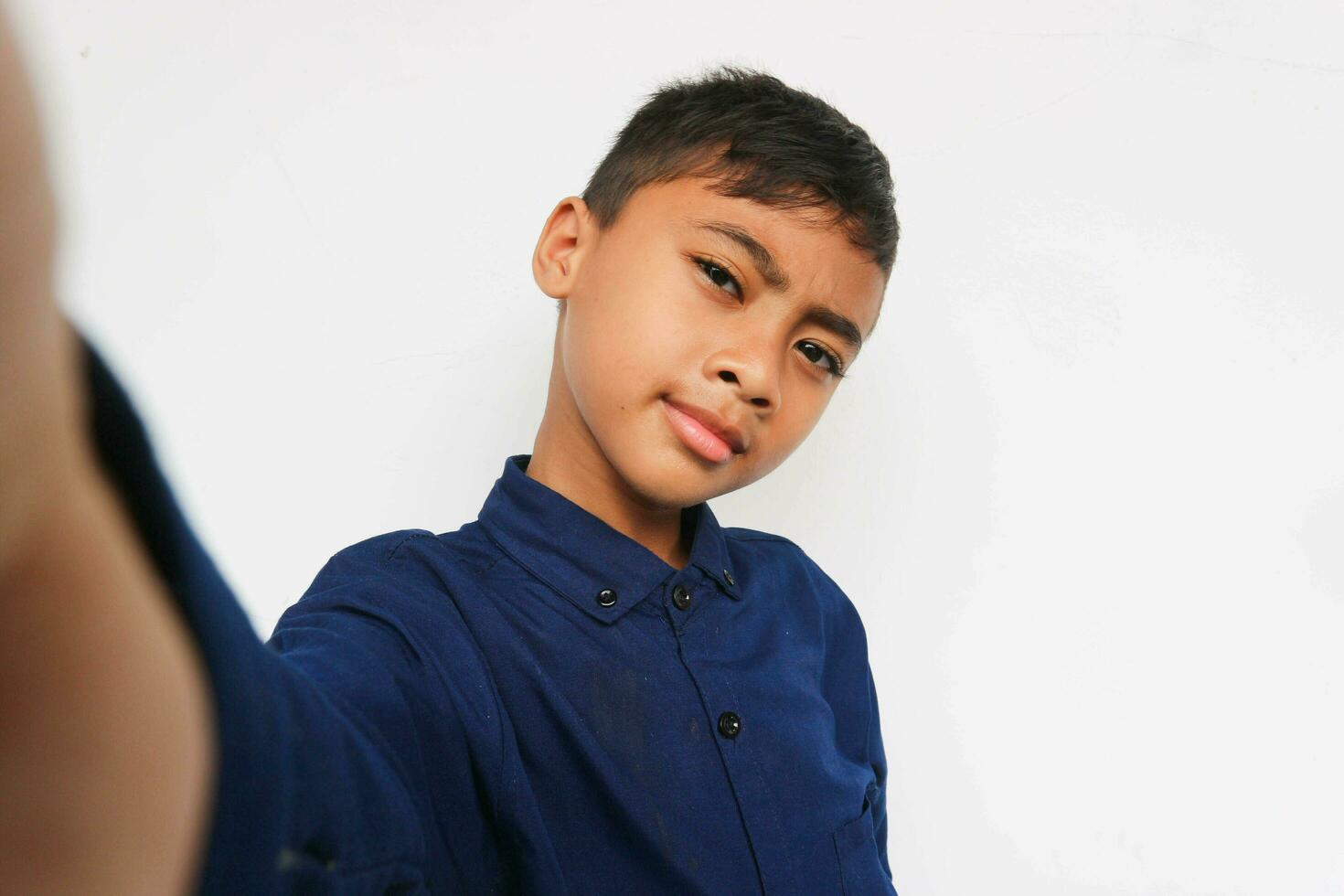 Cute little boy taking selfie on light background. Happy little boy with healthy teeth taking selfie. Photo of boy takes selfie with smart phone indoors. Boy takes selfie