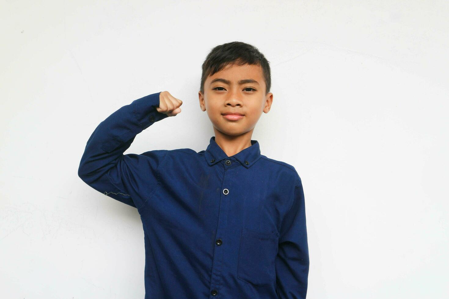 Asian boy in blue shirt demonstrating his muscles or biceps on the white background. Future and dream concept photo