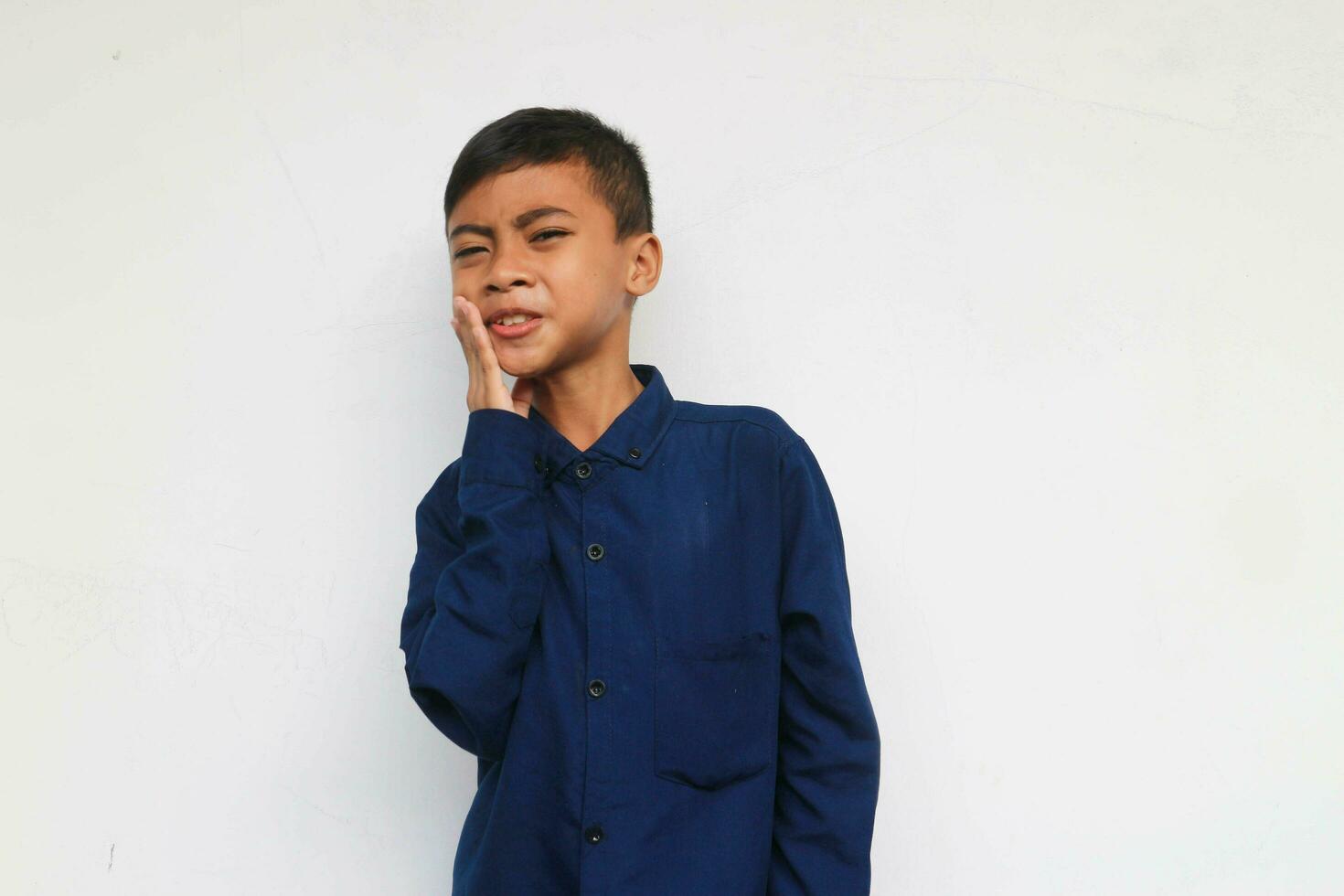 A boy with blue shirt is feeling unbearable toothache by holding his cheek photo