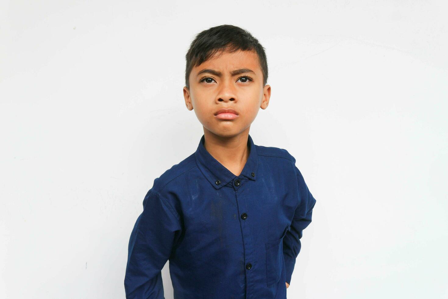 Angry boy wearing a blue shirt looking at the camera with serious face. Isolated on white background photo