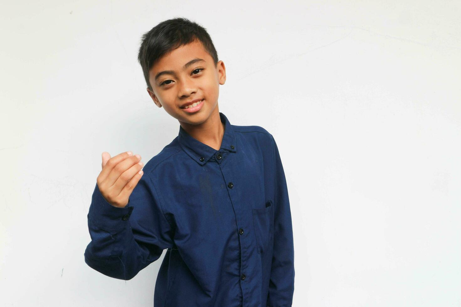 Smiling confident boy wearing a blue casual shirt looking at the camera while do inviting gesture by hand. Isolated on white background photo