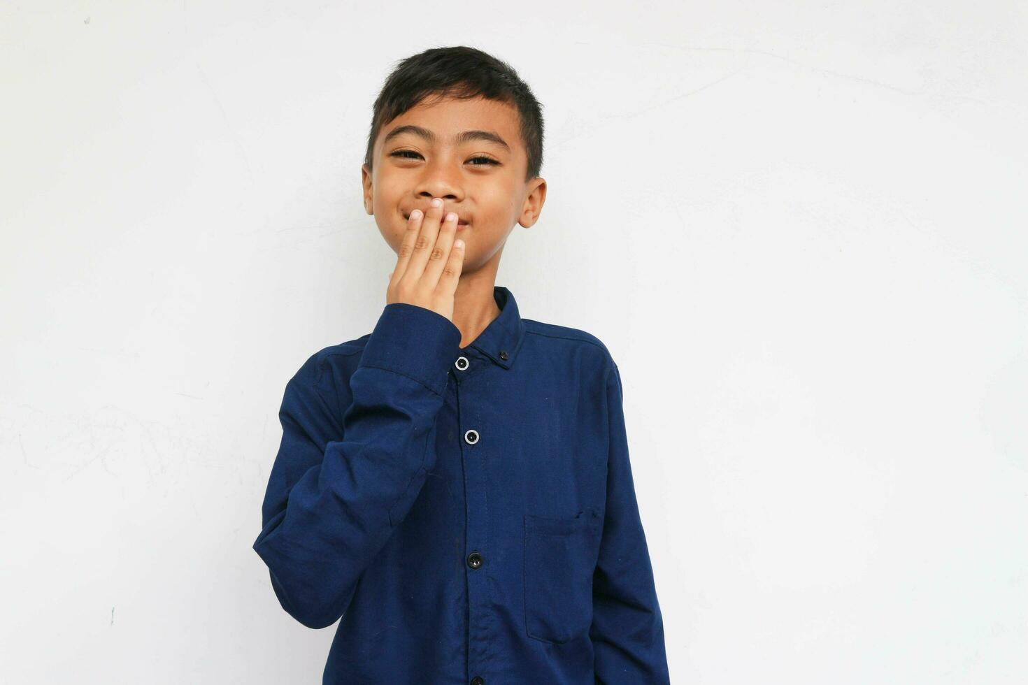 Smiling boy looking at camera while covering his mouth with hand in embarrassment photo