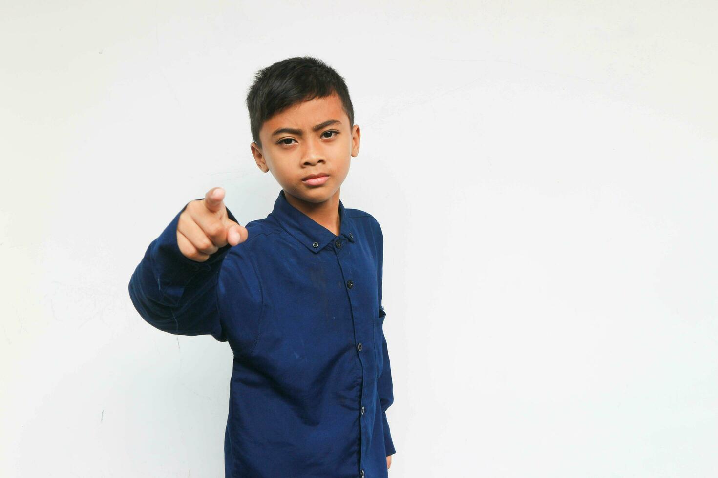 Angry boy wearing a blue shirt looking at the camera while pointing by hand. Isolated on white background photo