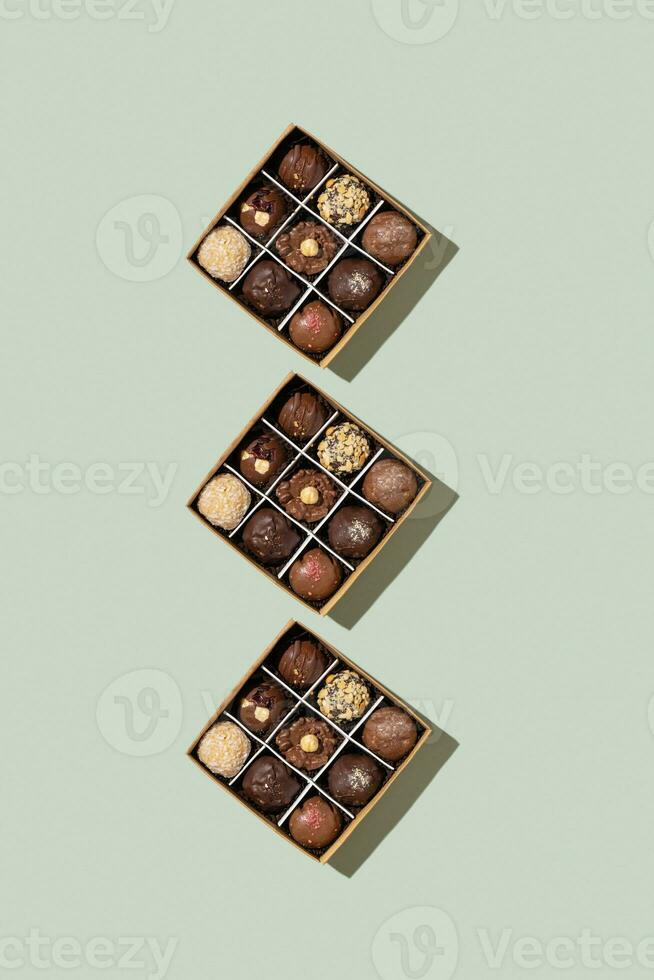 Pattern with box with chocolate craft candies with nuts inside on green background top view, flat lay photo