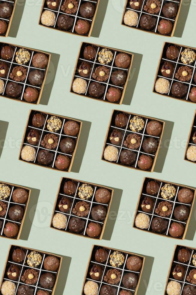 Pattern with box with chocolate craft candies with nuts inside on green background top view, flat lay photo