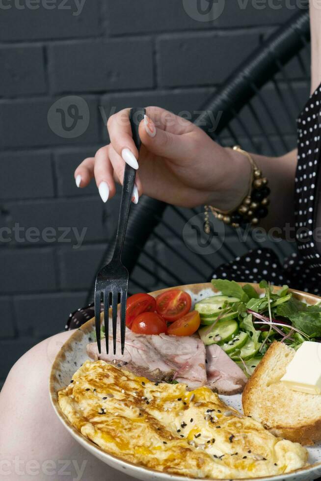 A plate with an omelette with turkey and vegetables. Female hands with a fork photo