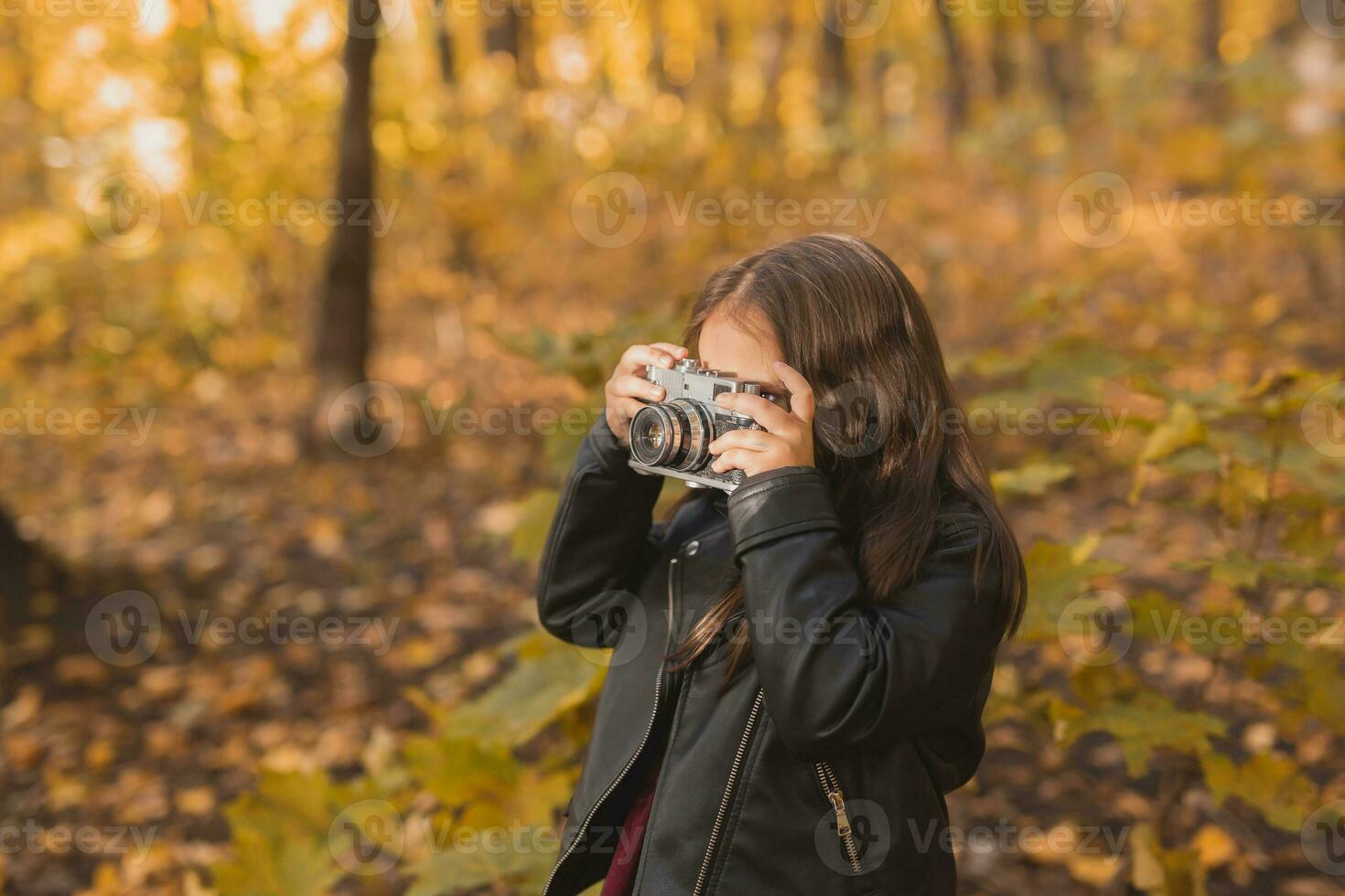 Child girl using an old-fashioned camera in autumn nature. Photographer, fall season and leisure concept. photo