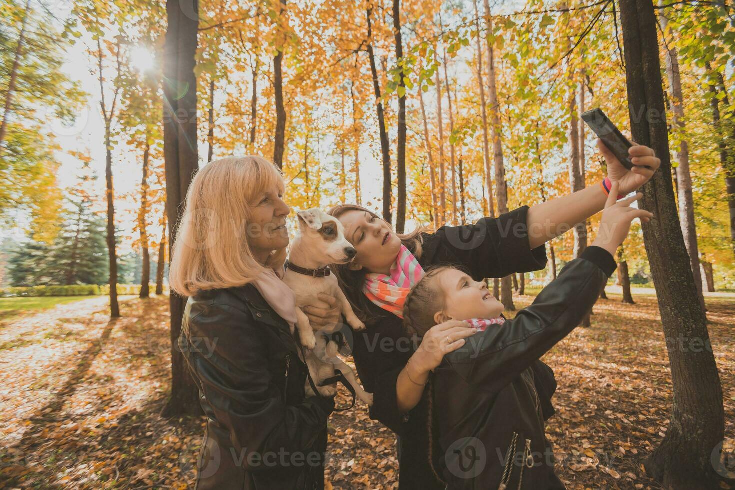 Three generations of women and dog feel fun look at camera posing for self-portrait picture together, funny excited child, mom and grandmother have fun enjoy weekend take selfie on gadget in autumn photo