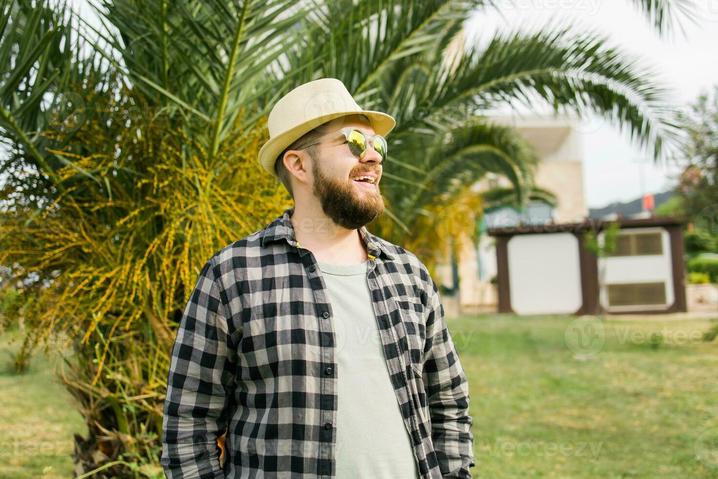 Laughing attractive man wearing hat over palm tree background with copy space - emotion and vacation travel holidays concept photo