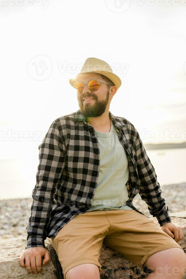 Handsome and confident. Outdoor portrait of smiling man wearing hat and sunglasses on beach. Holidays travel and summer tourism photo