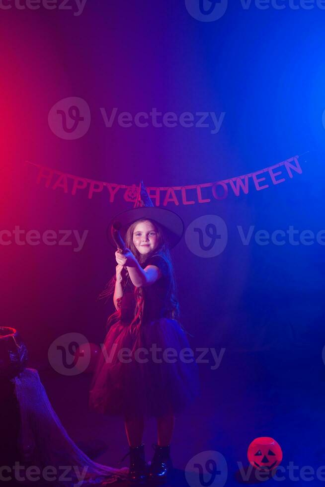 Little girl holds broom on Halloween holiday. Kid girl wear witch costume. Fantasy, fairy tale and masquerade concept. photo