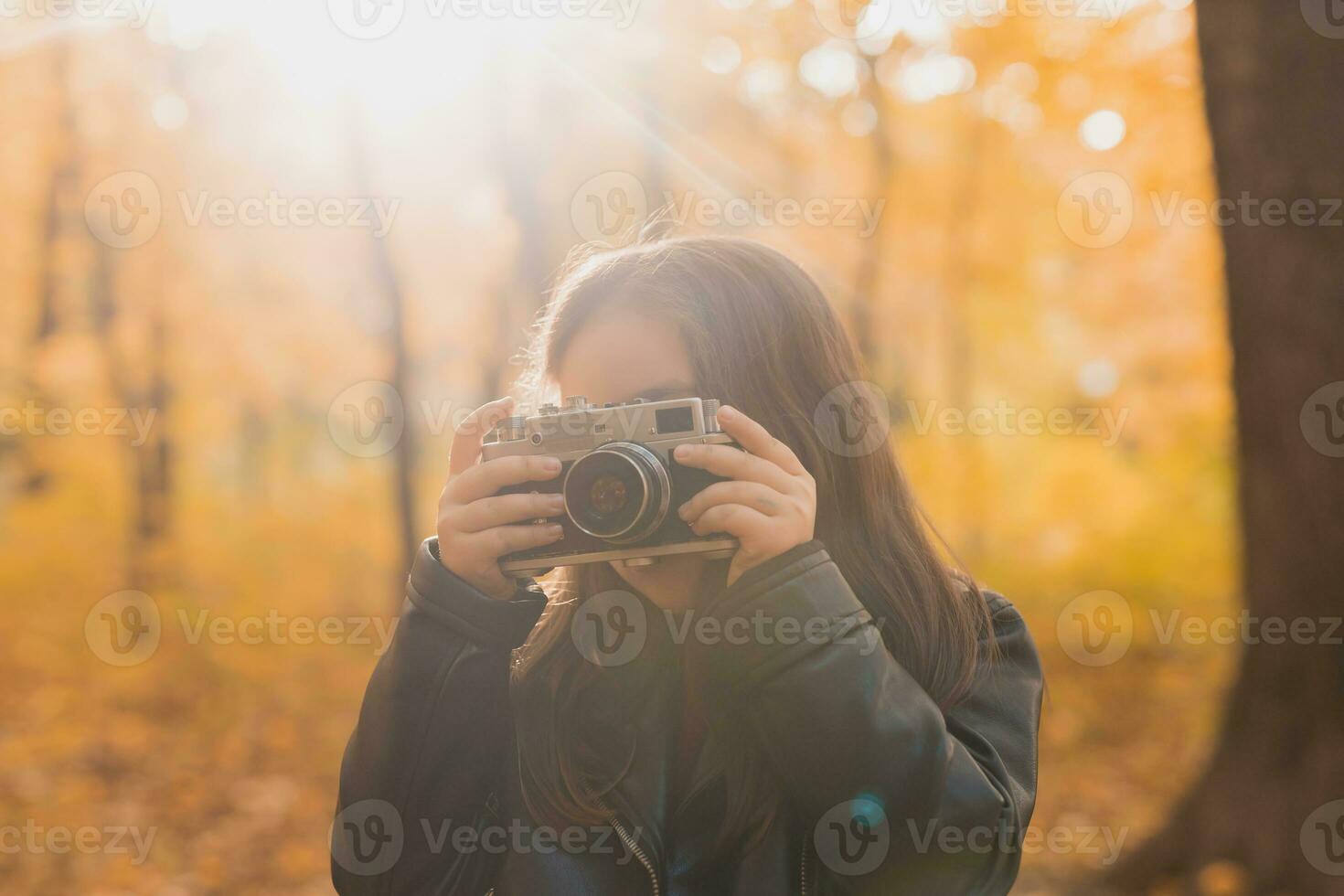 A little girl take a photo with old retro camera in autumn nature. Leisure and hobby concept.