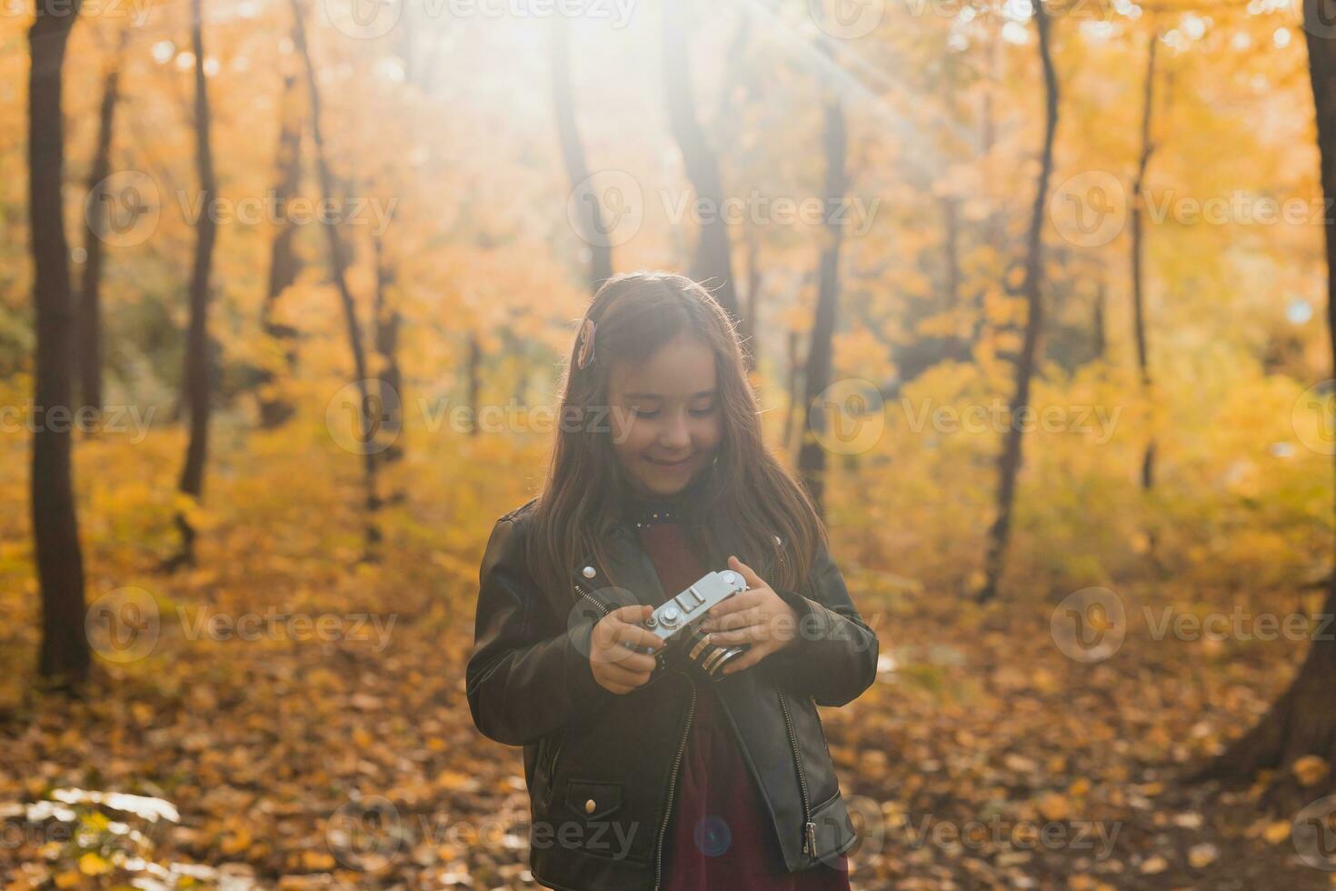 niño niña utilizando un Anticuado cámara en otoño naturaleza. fotógrafo, otoño temporada y ocio concepto. foto