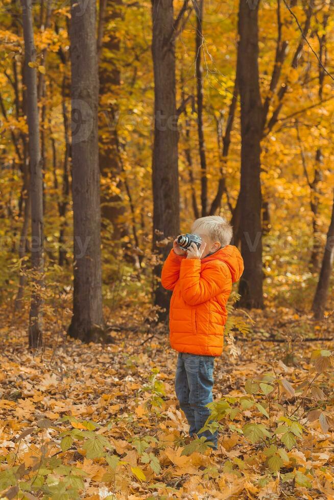 Boy with retro camera taking pictures outdoor in autumn nature. Leisure and photographers concept photo