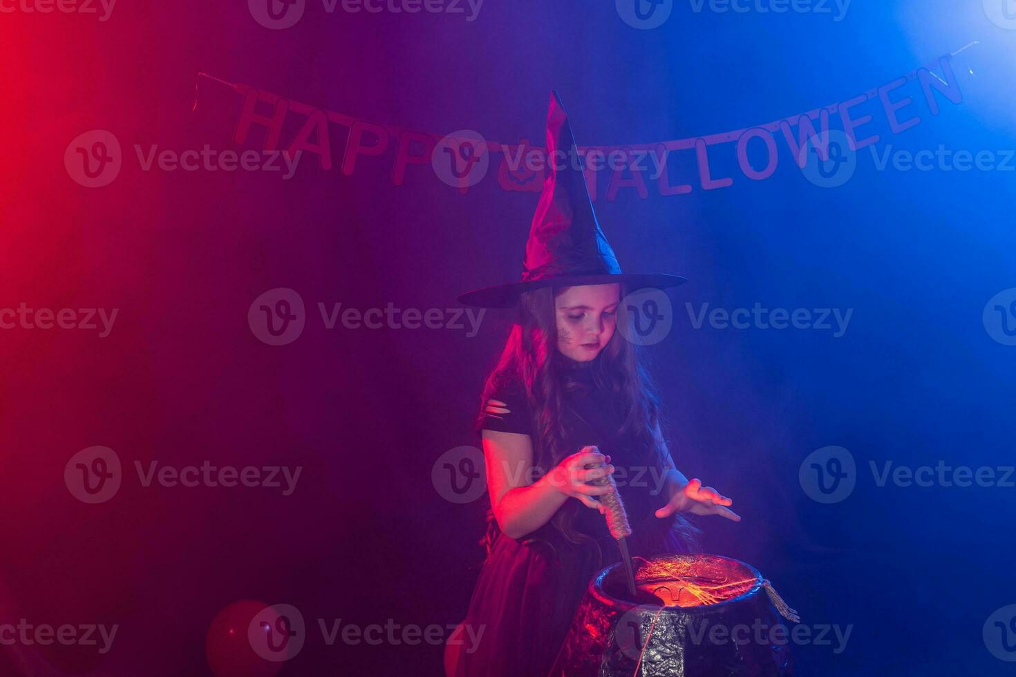 Little witch child cooking potion in the cauldron on Halloween. photo