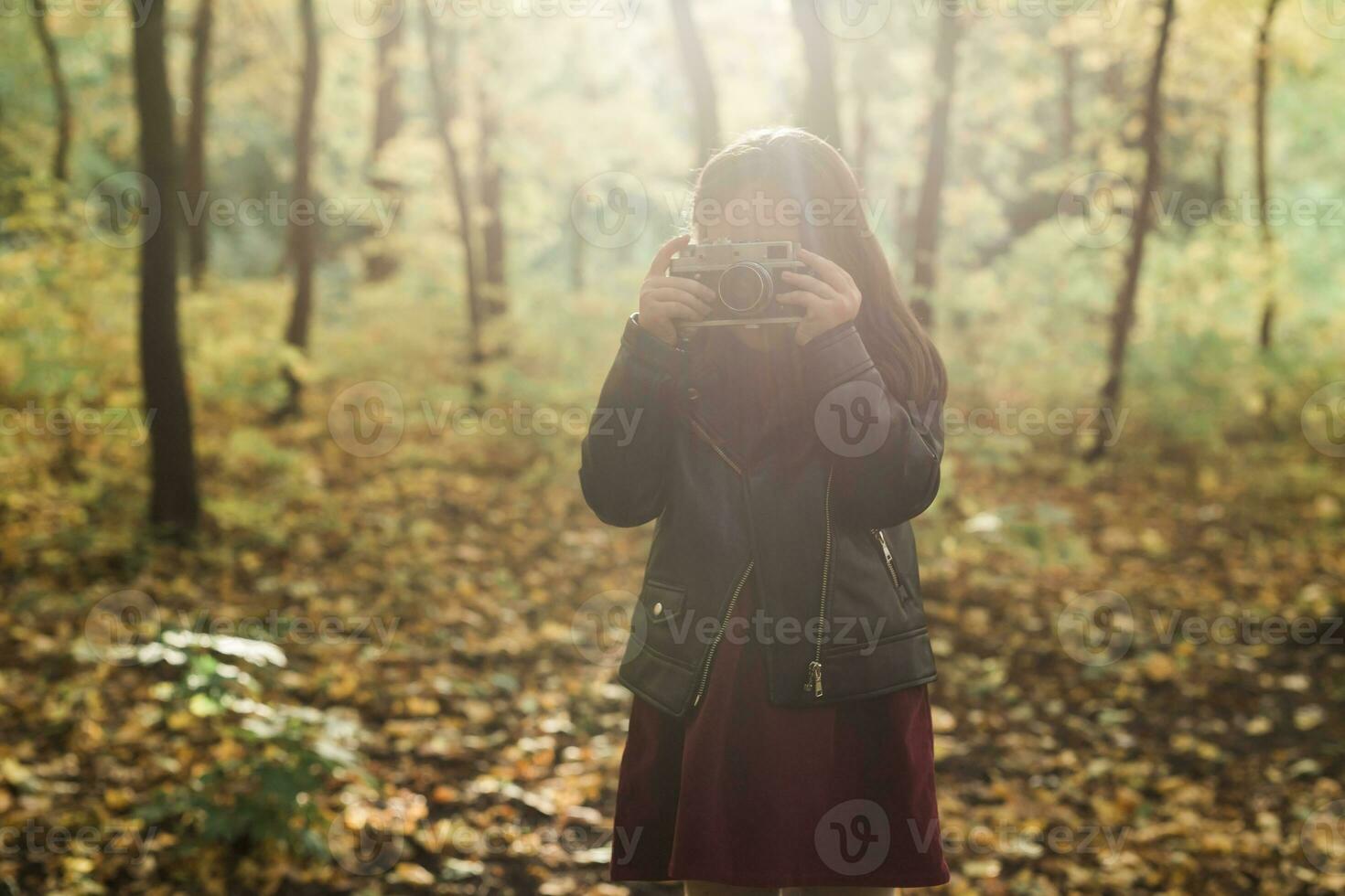 A little girl take a photo with old retro camera in autumn nature. Leisure and hobby concept.