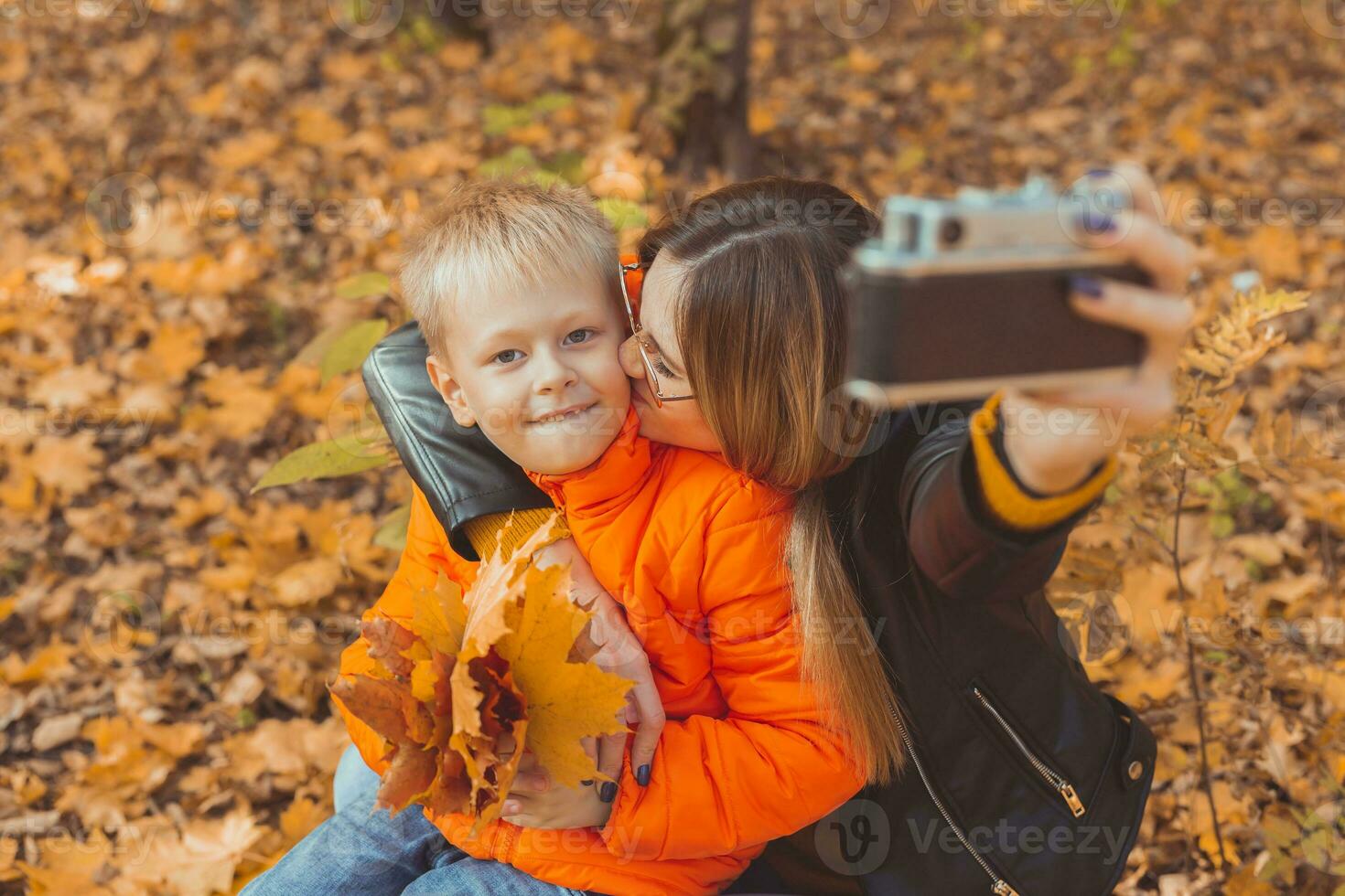 Son and mother are taking selfie and having fun in autumn park. Single parent, leisure and fall season concept. photo