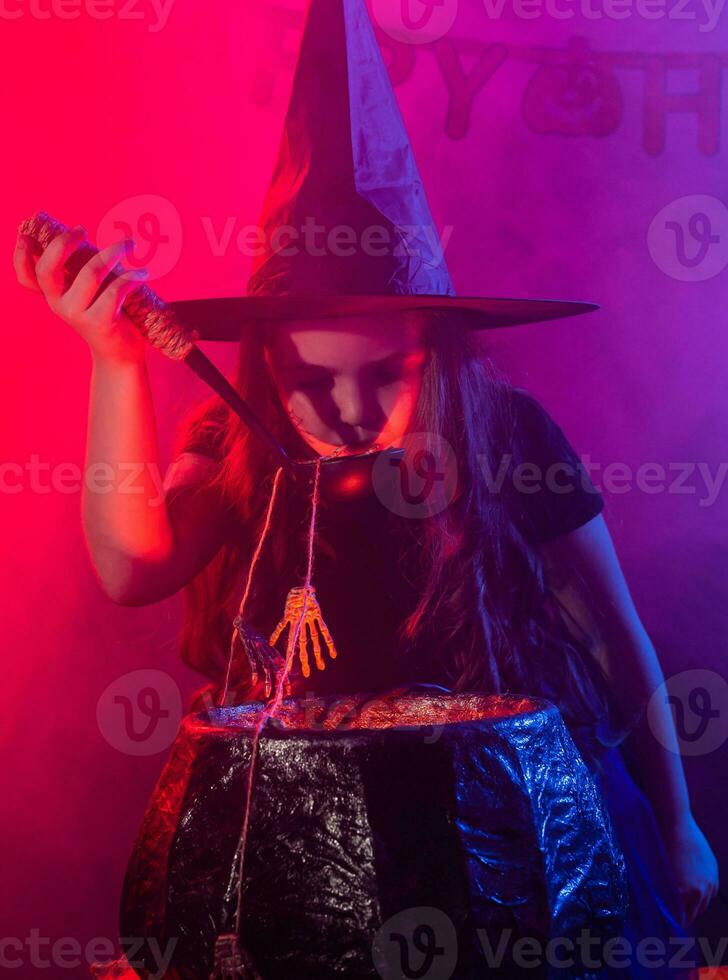 Child girl witch preparing a potion in the cauldron at halloween holidays. photo