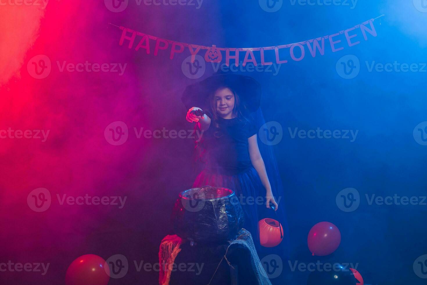 Child girl witch preparing a potion in the cauldron at halloween holidays. photo