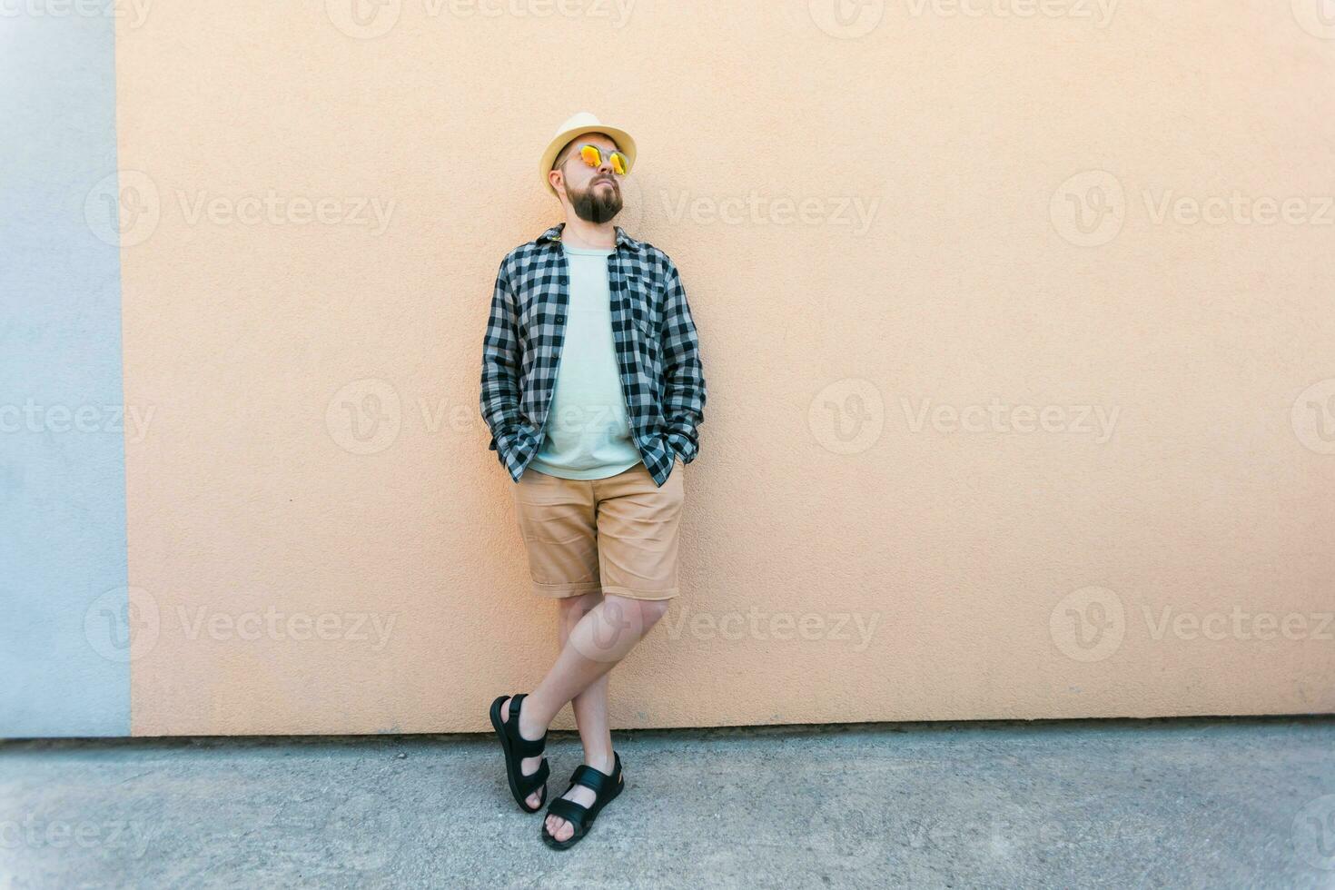Bearded man in summer clothes and hat stand over beige wall on street city urban and travel concept - copy space and empty space for advertising photo
