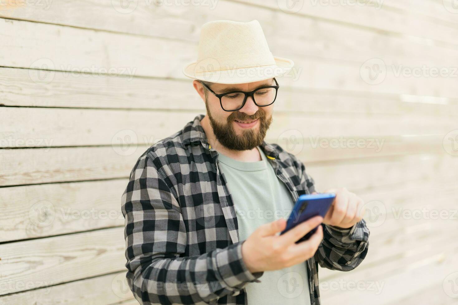 Smiling male tourist use smartphone during summer city break over wooden wall - technologies and social media app concept photo