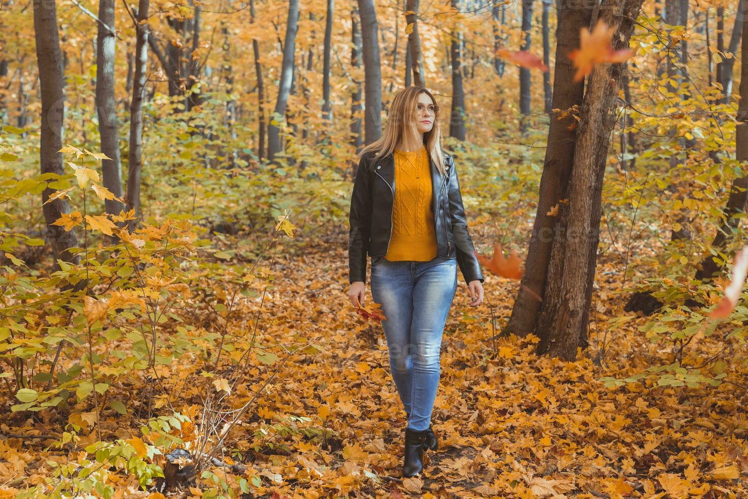 Cute smiley woman holding autumn leaves and walks in fall park. Seasonal, lifestyle and leisure concept. photo