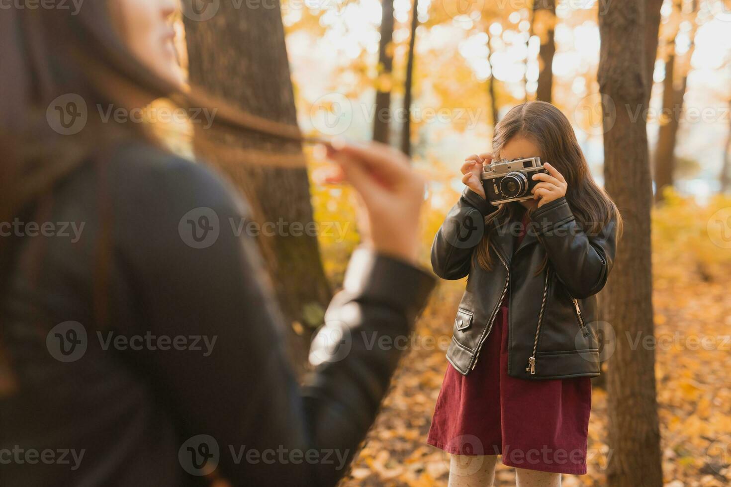 Child taking picture her mother on retro camera in autumn park. Hobbies and leisure concept. photo