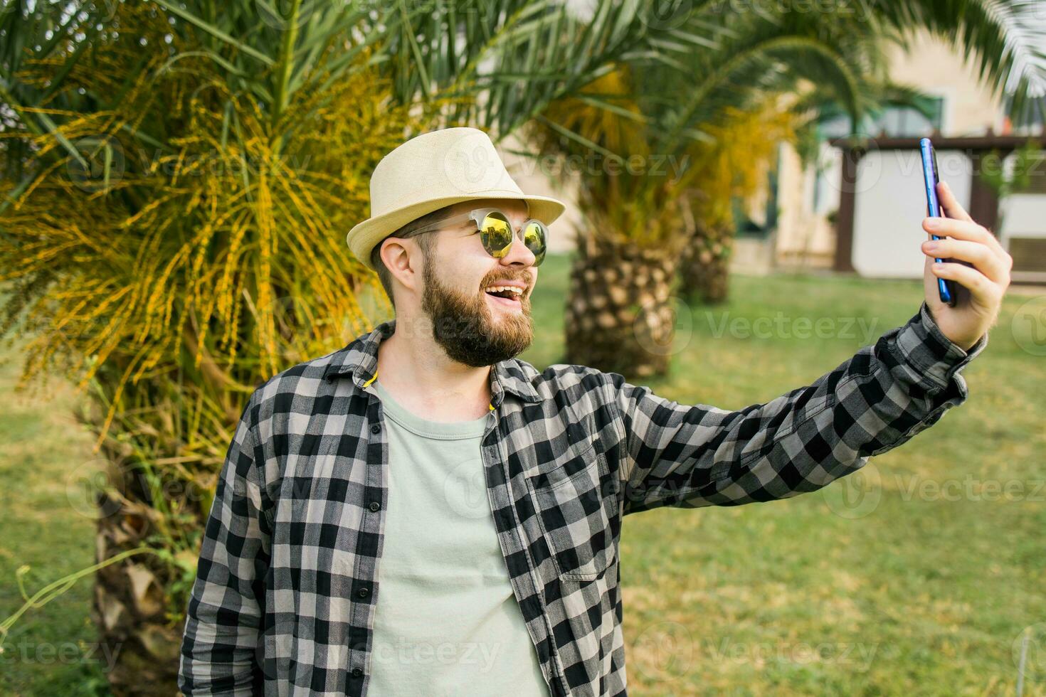 Man taking selfie portrait over palm tree background - Happy millennial guy enjoying summer holidays in city - Youth and technologies photo