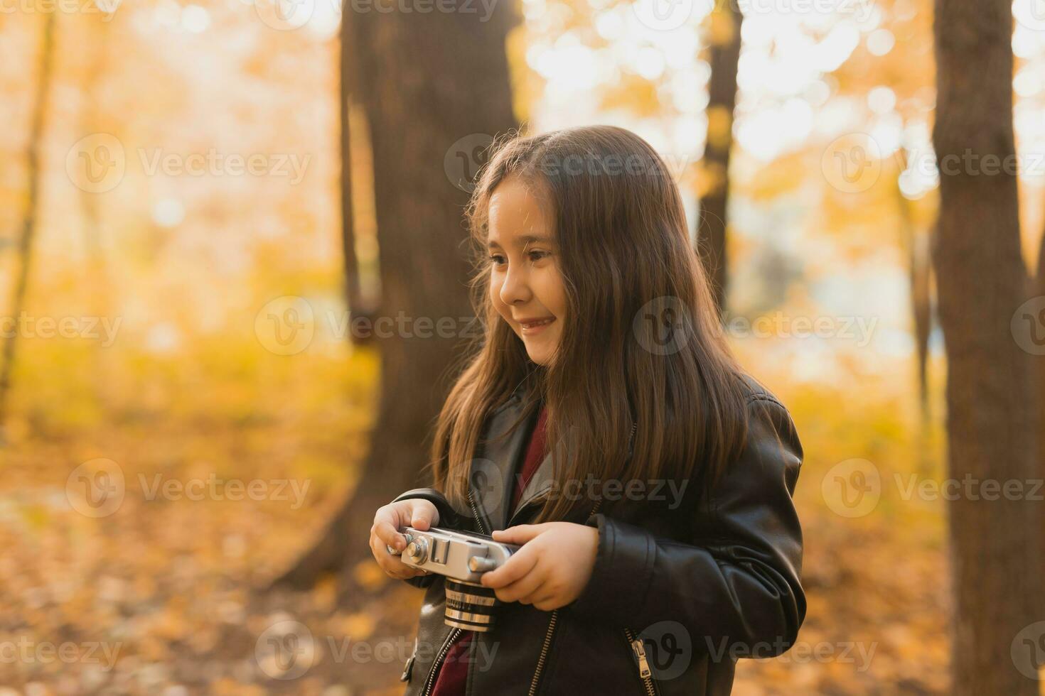 un pequeño niña tomar un foto con antiguo retro cámara en otoño naturaleza. ocio y pasatiempo concepto.