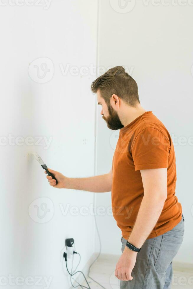 Man smoothes wall surface with a wall grinder. Male grind a white plaster wall - renovation and redecoration concept photo