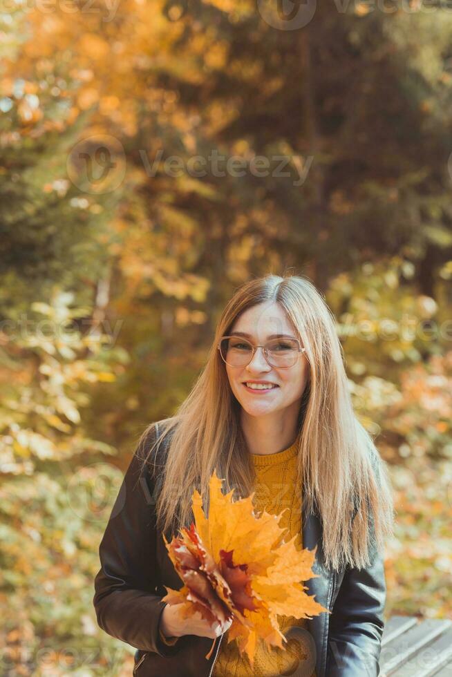 Cute smiley woman holding autumn leaves in fall park. Seasonal, lifestyle and leisure concept. photo
