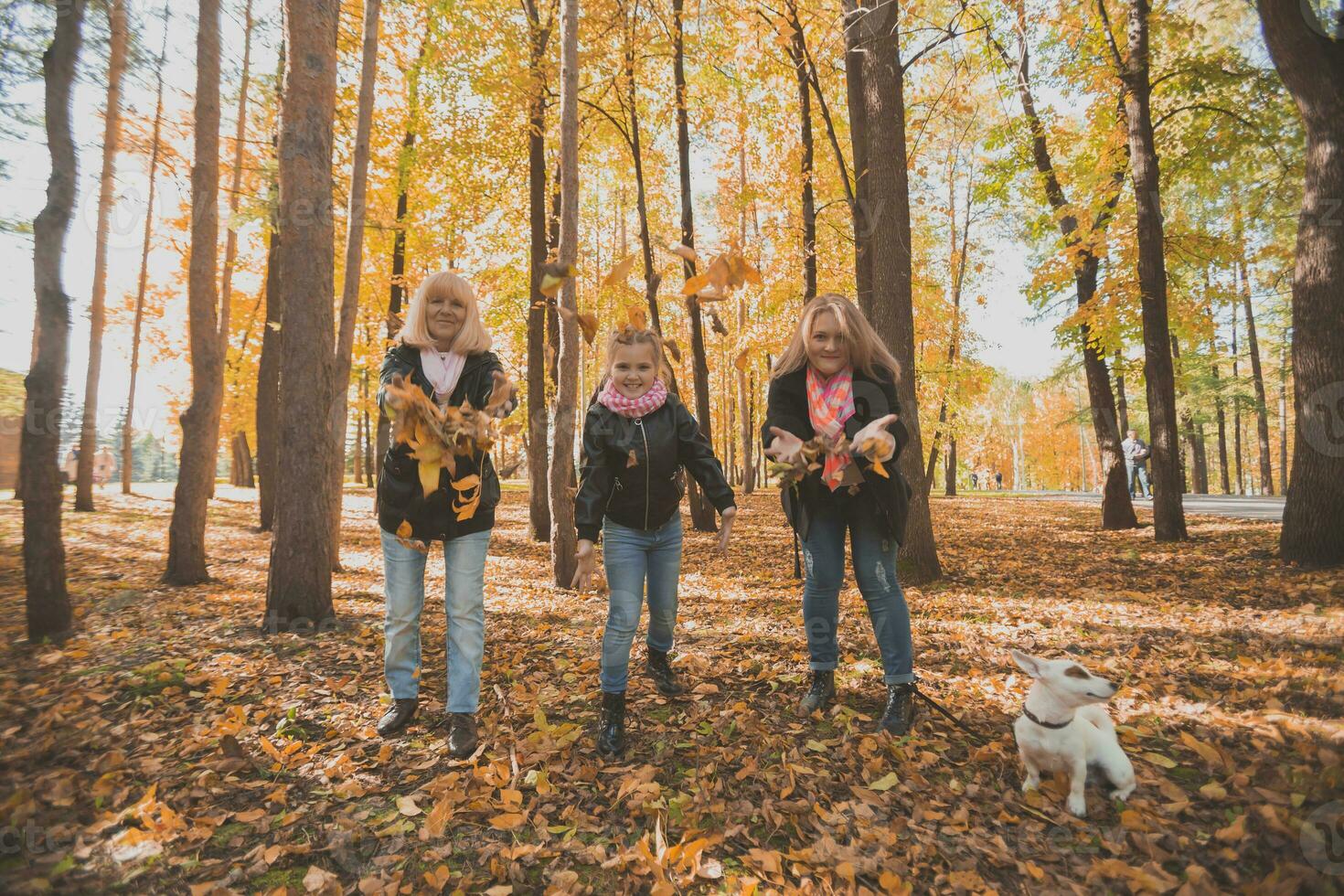 Grandmother and mother with granddaughter throw up fall leaves in autumn park and having fun. Generation, leisure and family concept. photo