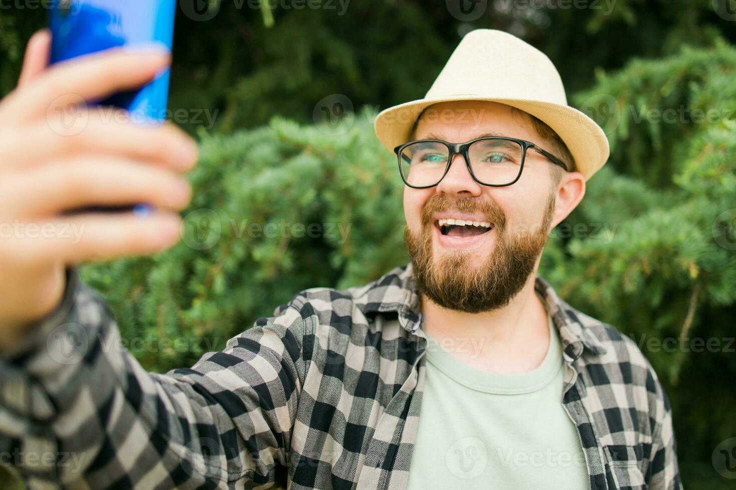 Man taking selfie portrait over tree background - Happy millennial guy enjoying summer holidays in city - Youth and technologies photo