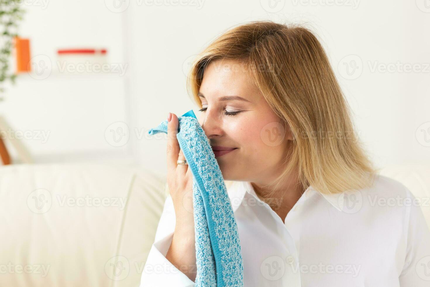 Beautiful woman is smelling clean towels and smiling while doing laundry at home - fabric softener concept photo