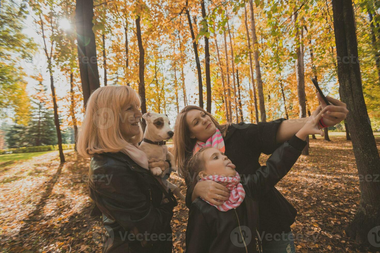 Three generations of women and dog feel fun look at camera posing for self-portrait picture together, funny excited child, mom and grandmother have fun enjoy weekend take selfie on gadget in autumn photo