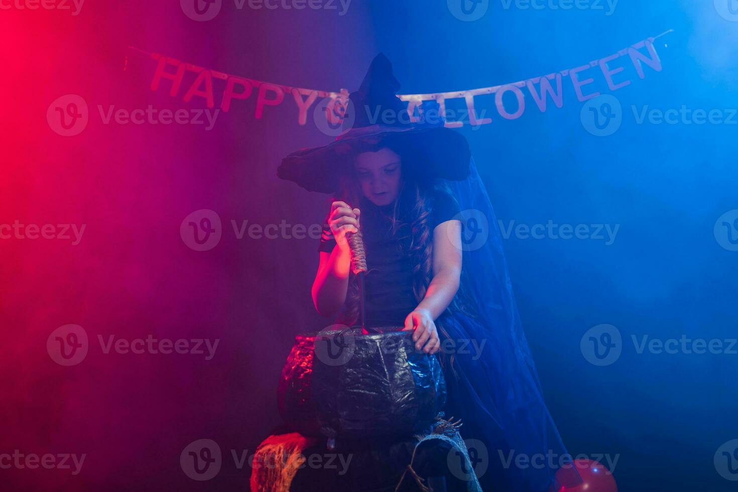 Child girl witch preparing a potion in the cauldron at halloween holidays. photo