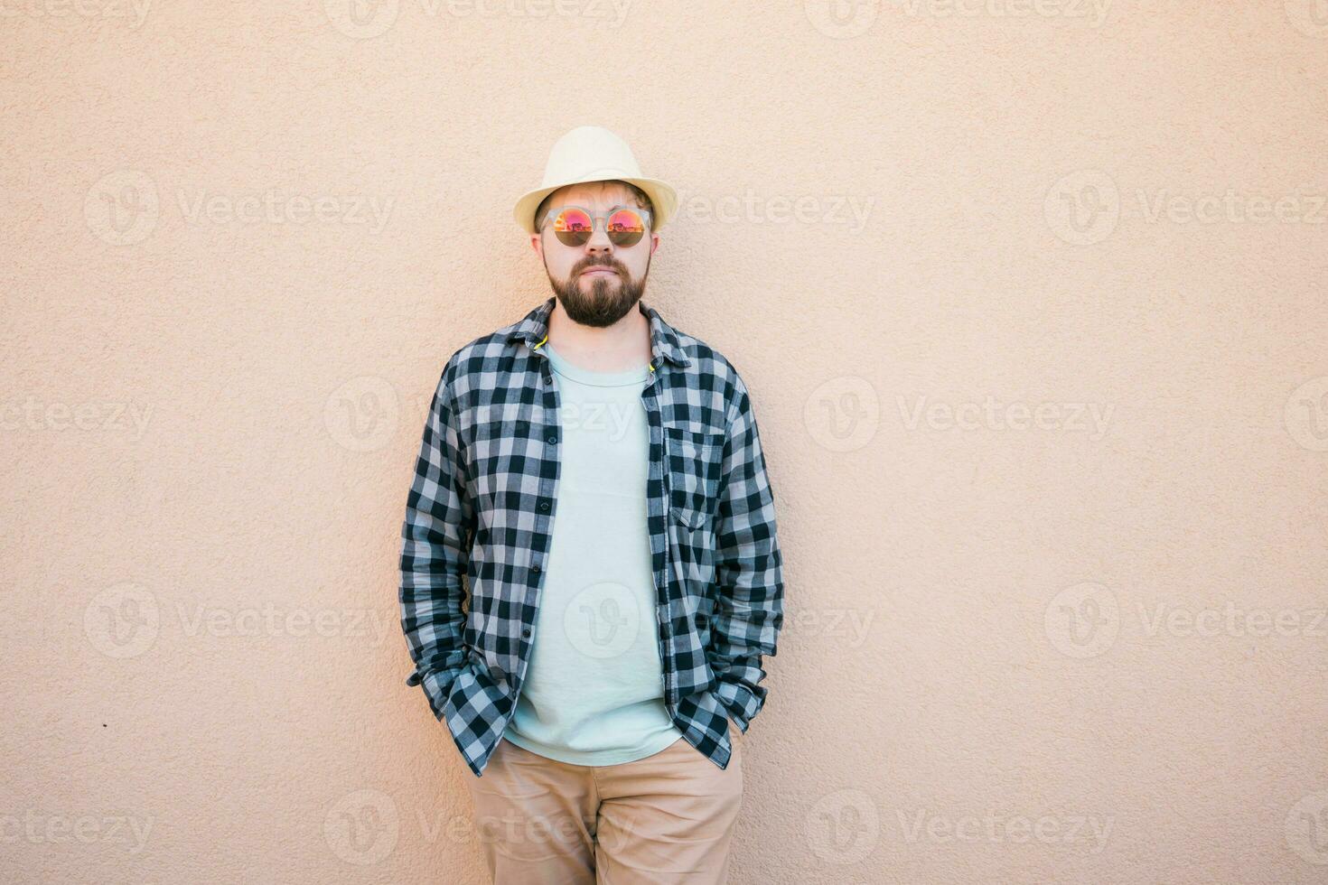 Handsome caucasian man wearing summer hat and plaid shirt smiling happy near wall with copy space - travel vacations and summer holiday concept photo