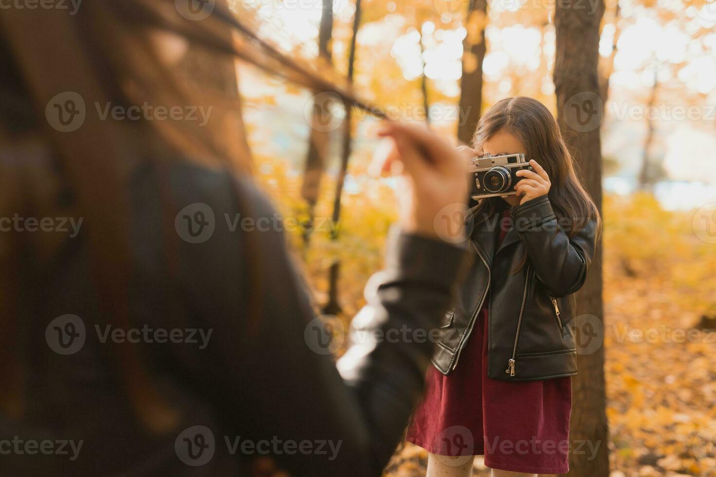 Child taking picture her mother on retro camera in autumn park. Hobbies and leisure concept. photo