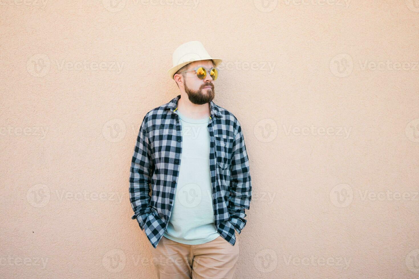 Bearded man in summer clothes and hat stand over beige wall on street city urban and travel concept - copy space and empty space for advertising photo