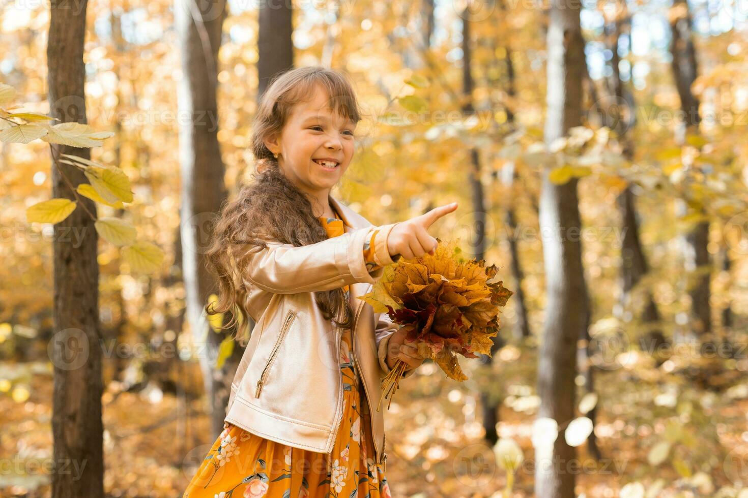 Little kid girl with autumn orange leaves in a park. Lifestyle, fall season and children concept. photo