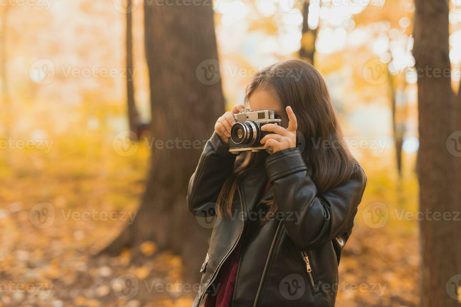Child girl using an old-fashioned camera in autumn nature. Photographer, fall season and leisure concept. photo