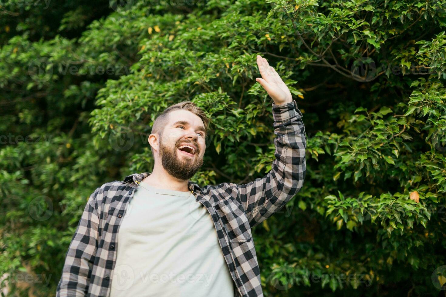 Side view of delighted male standing outdoors and waving hand to his friend. He is joyful to meet his acquainted by chance. Copy space and place for advertising photo