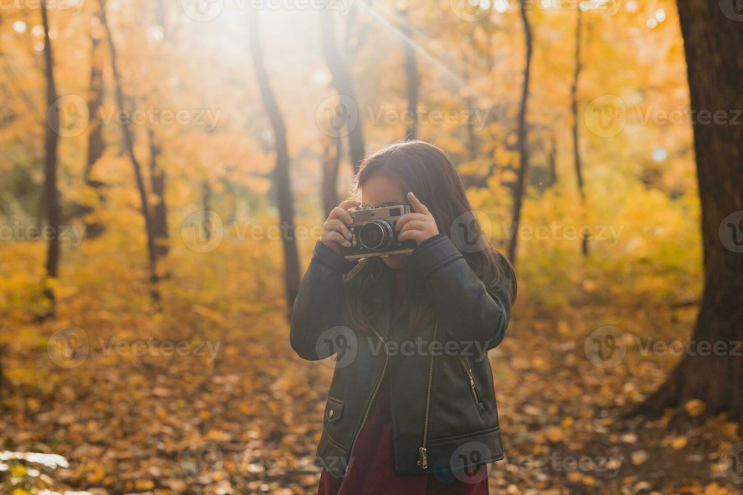 A little girl take a photo with old retro camera in autumn nature. Leisure and hobby concept.