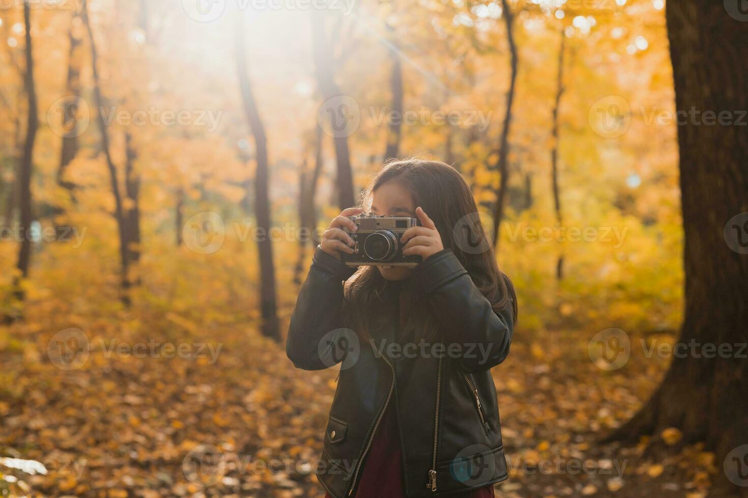 A little girl take a photo with old retro camera in autumn nature. Leisure and hobby concept.